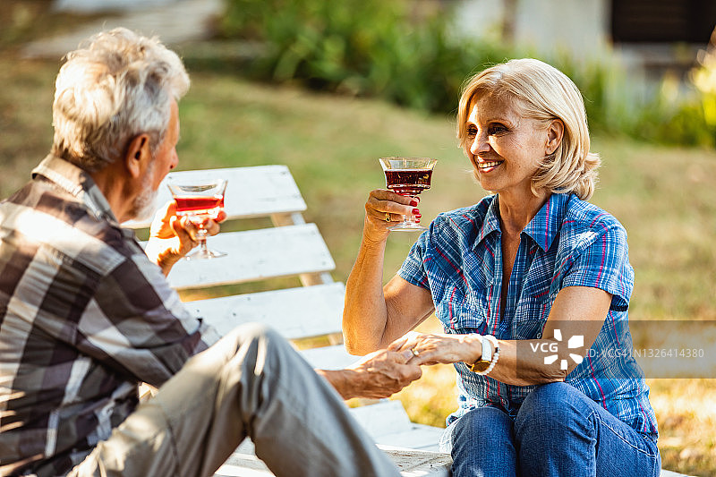 老人和女人在一起喝酒。一对老夫妇坐在一个花园里，手拿酒杯，面面相觑。图片素材