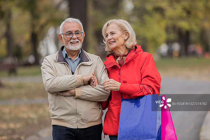 一对快乐的老人在逛完购物中心后在公园里散步。图片素材