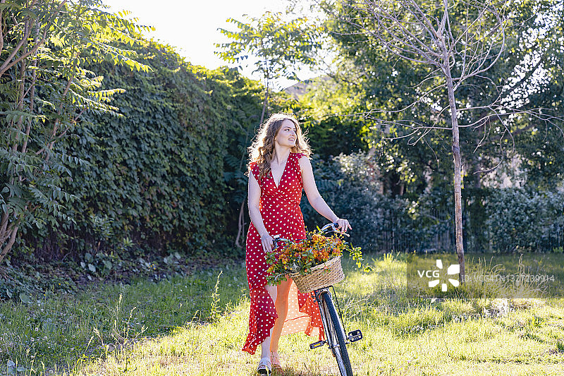 年轻女子在花园里推着自行车，看着别处图片素材