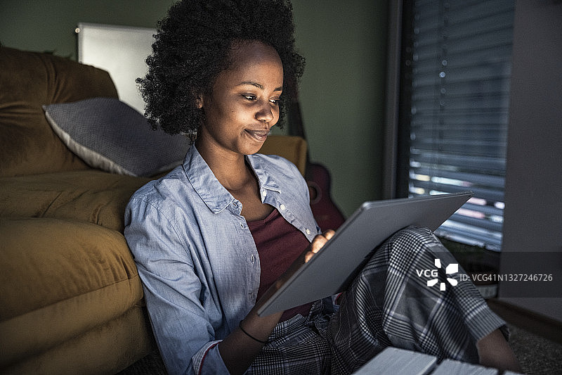 微笑的女人坐在客厅里使用数码平板电脑图片素材
