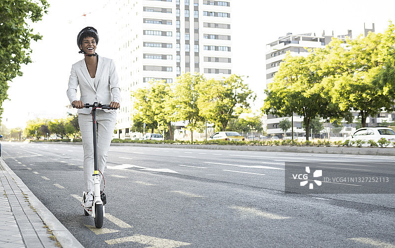 快乐的女性通勤骑电动车在城市的街道上图片素材