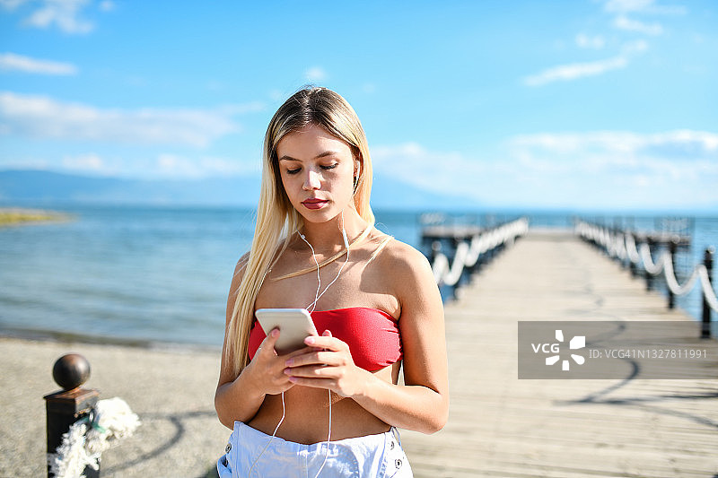 在海滩上用智能手机听音乐的平静女性美丽图片素材