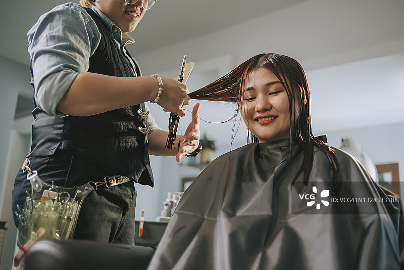 亚洲华人女发型师在发廊为她的顾客梳理光滑的长发图片素材