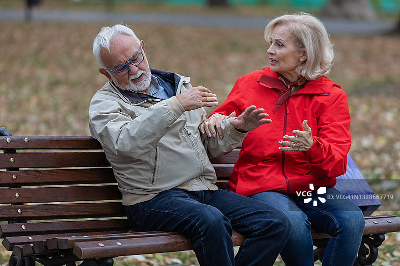 一对不高兴的老年人坐在城市公园里讨论他们遇到的问题。图片素材