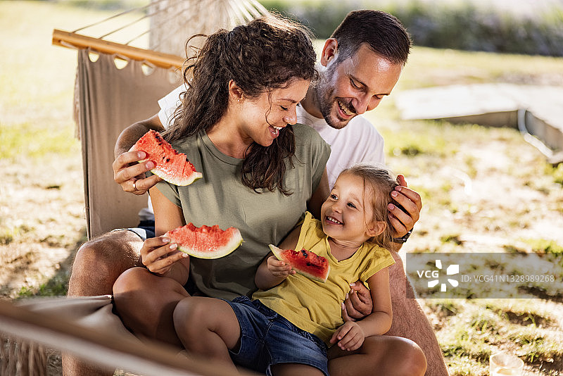 幸福的一家人在后院的吊床上吃西瓜。图片素材