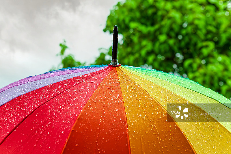 彩虹伞上的雨。雨伞下着大雨，映衬着阴天的背景。图片素材