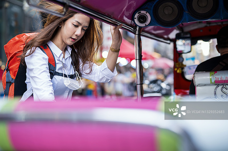 亚洲女性背包客在泰国曼谷的考山路上坐上嘟嘟车。在泰国旅行时，嘟嘟车是必做的事情之一。图片素材