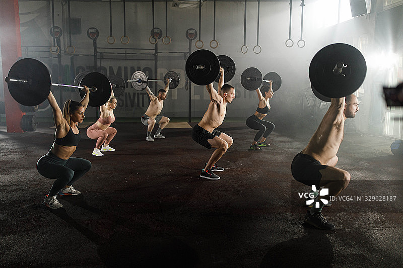 一群运动员在健身房用杠铃锻炼。图片素材