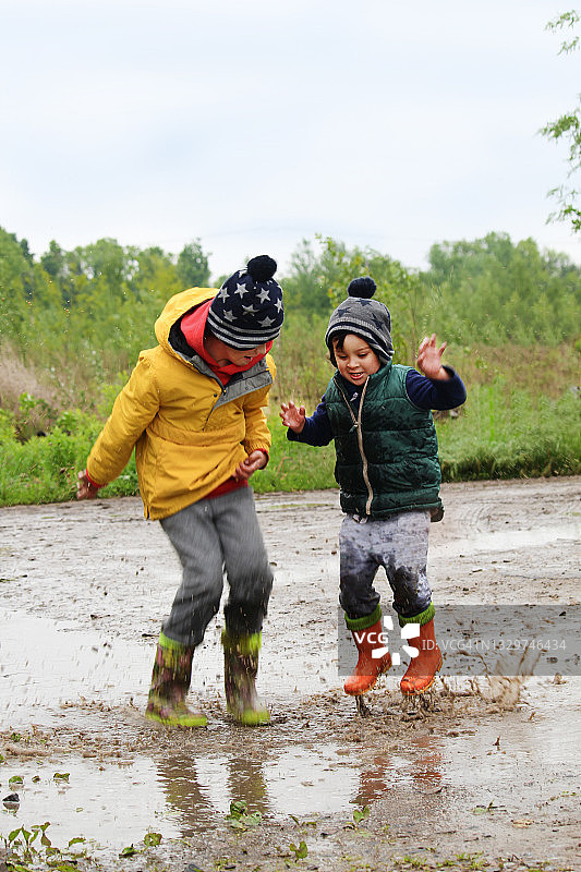 两个男孩在泥泞的水坑里跳图片素材
