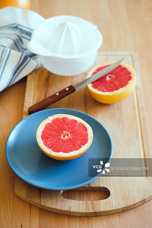 红色成熟的葡萄柚，切成两半，放在案板上，背景是木制的厨房桌子。旁边是一个手动榨汁机，用来榨汁。素食、纯素食和生食的概念。图片素材