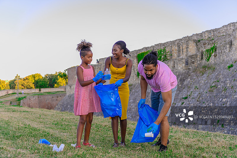 一个快乐的非裔美国家庭正在草地上捡垃圾。图片素材