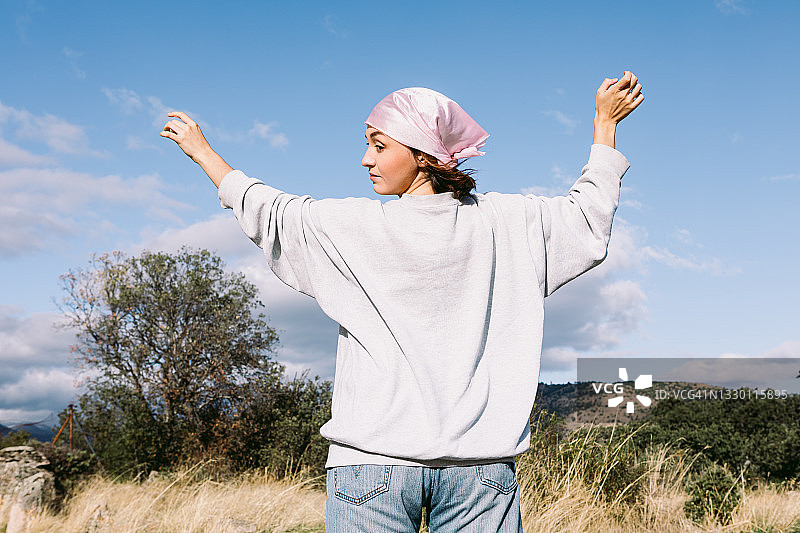 田野里的小女孩背对着她的头，戴着粉红色的围巾，国际乳腺癌日，背景是天空。乳腺癌的概念图片素材