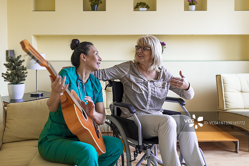 一位女性家庭护理员正在给一位坐在轮椅上的老妇人弹吉他。图片素材