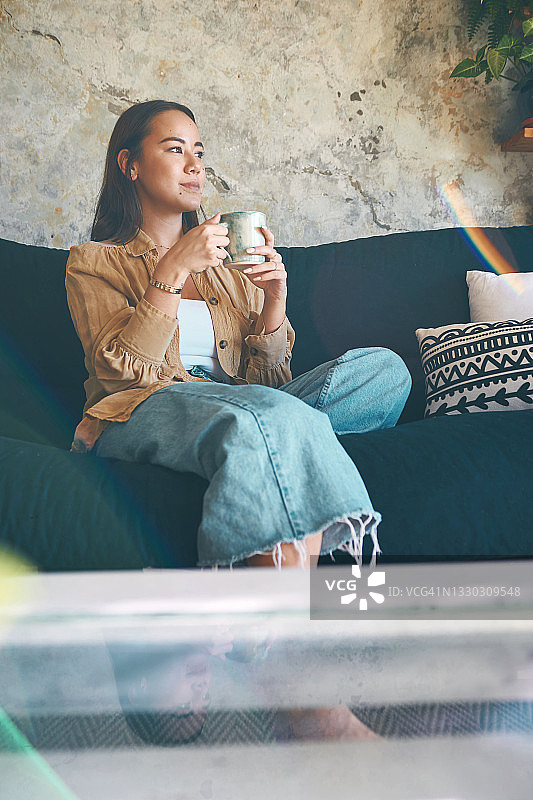 一个年轻女人在家喝咖啡，在沙发上放松图片素材