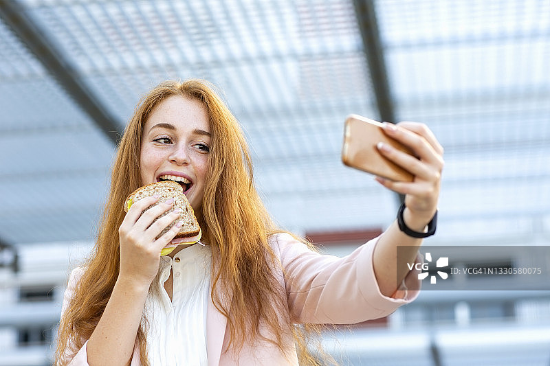 红发女商人一边吃三明治一边用手机自拍图片素材