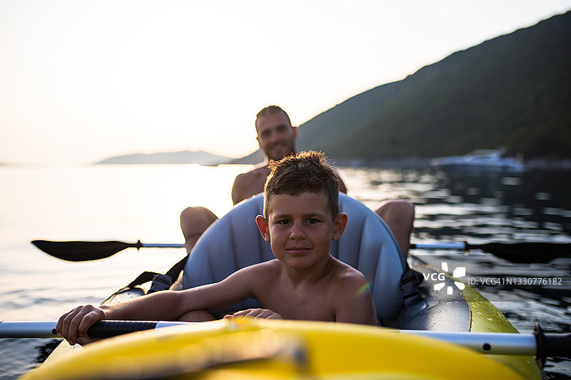 一个男孩和他爸爸在日落时分划皮艇图片素材
