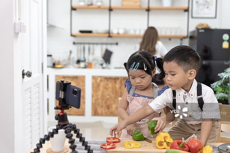 两个亚洲孩子一起做饭，并在家里的厨房录制教程自制烹饪的视频图片素材