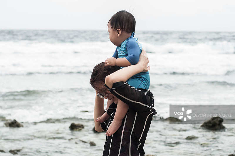 一位东南亚母亲背着儿子走在沙滩上图片素材
