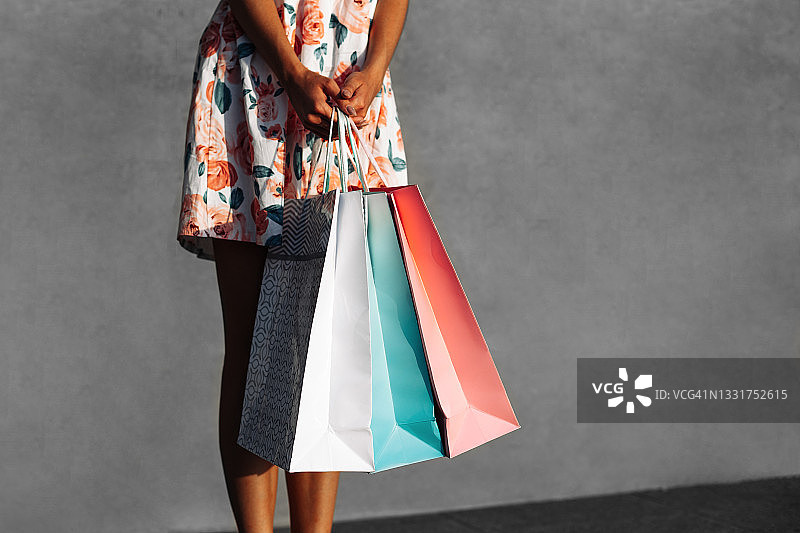 快乐购物，女人拿着购物袋的裁剪视图，女人在明亮的夏装拿着五颜六色的袋子，在城市的灰色墙壁图片素材