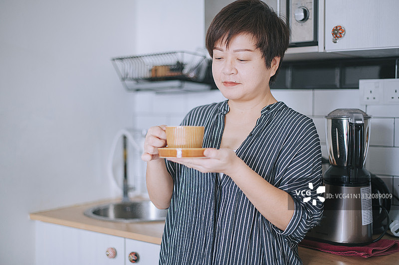 亚洲的中国成熟女性在厨房休息喝咖啡早餐，在清新的早晨上班前提神醒脑图片素材