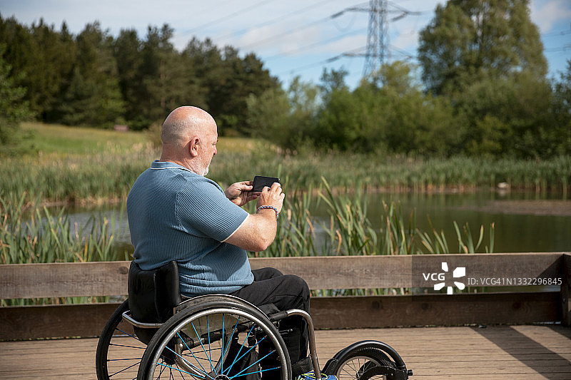 一个坐在轮椅上的成熟男人用智能手机拍照图片素材