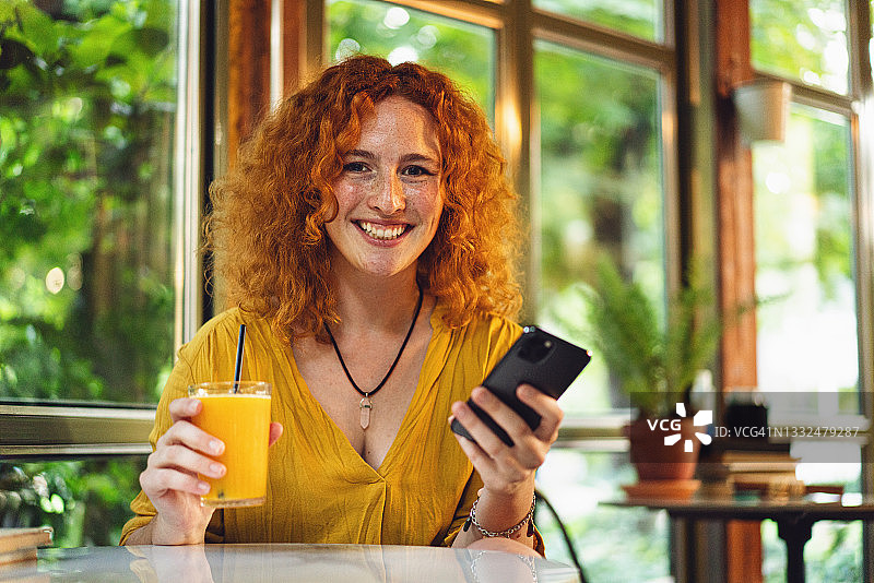 现代年轻女子，在咖啡馆里享受着宁静的环境，在手机上上网，喝着橙汁提神图片素材