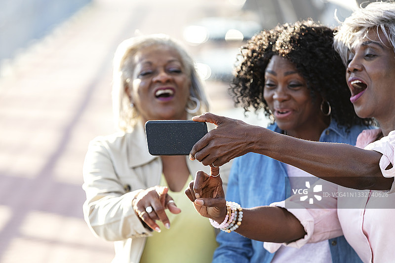 三位非裔美国妇女坐在公园长椅上，展示手机图片素材