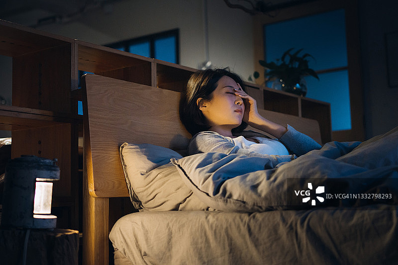 年轻的亚洲妇女感到不舒服，头痛，躺在床上，在家里休息图片素材