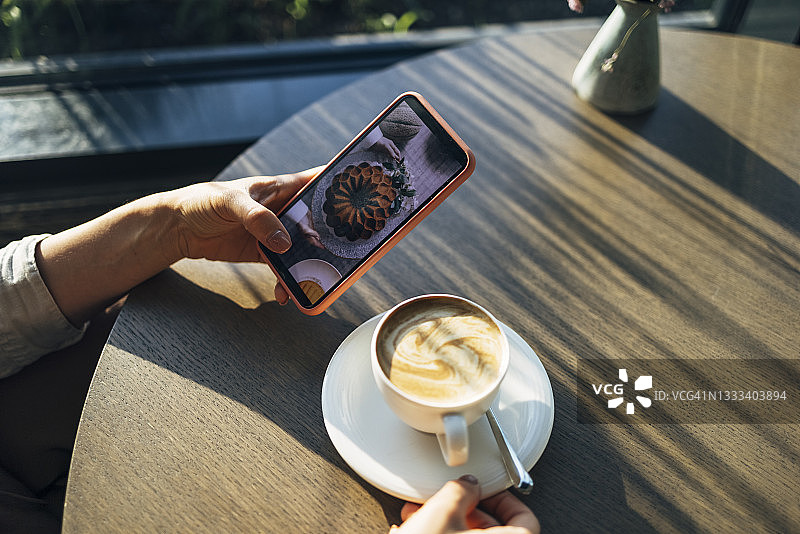 一位匿名女商人一边在咖啡馆喝咖啡，一边用手机看蛋糕的照片图片素材