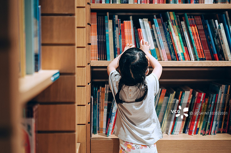 亚洲小女孩在图书馆的书架上挑选书籍图片素材
