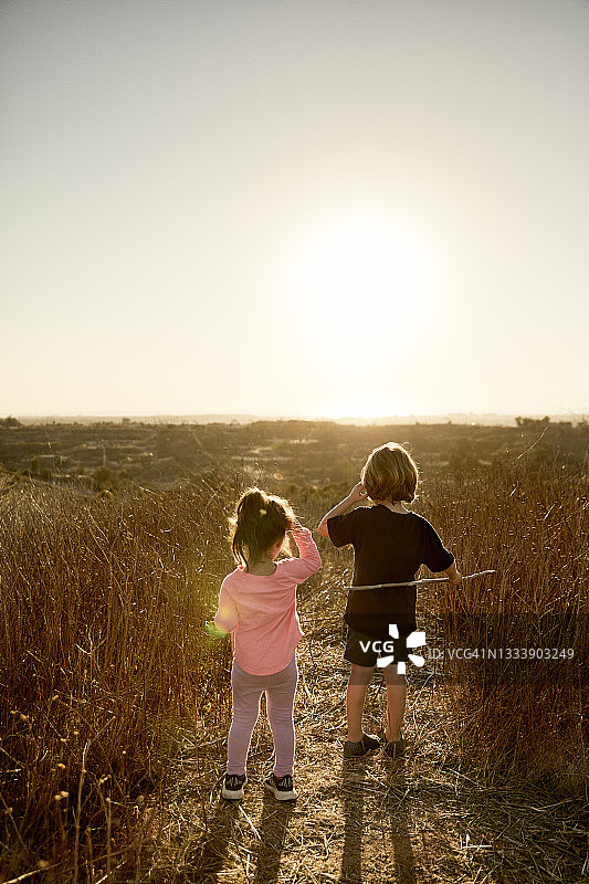 日出时兄弟姐妹站在田野上看风景的背面图片素材