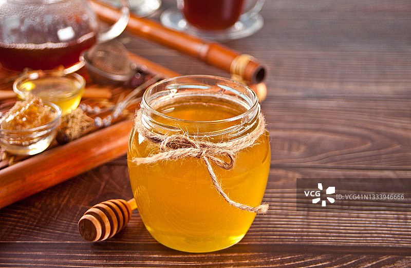 罐子里的蜂蜜和小碗里的蜂巢。背景上有茶壶和茶杯。图片素材