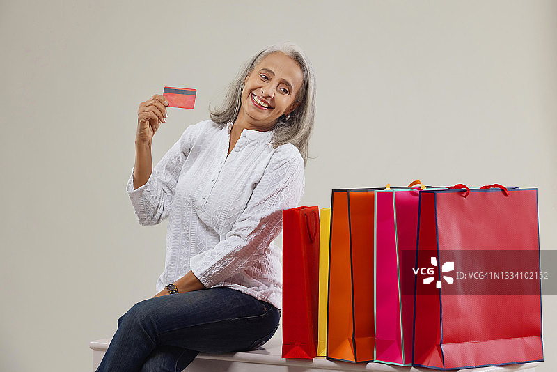 一位老妇人拿着信用卡高兴地看着她的行李。图片素材