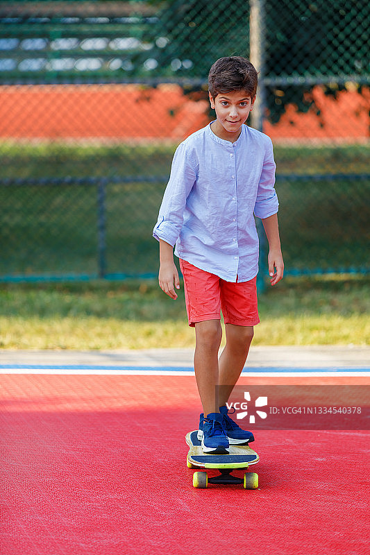 一个小男孩在公园里玩滑板。图片素材
