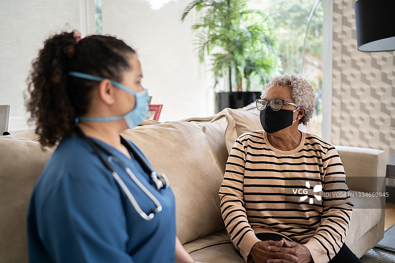 一位年长的妇女在家访期间戴着防护口罩与护士交谈图片素材