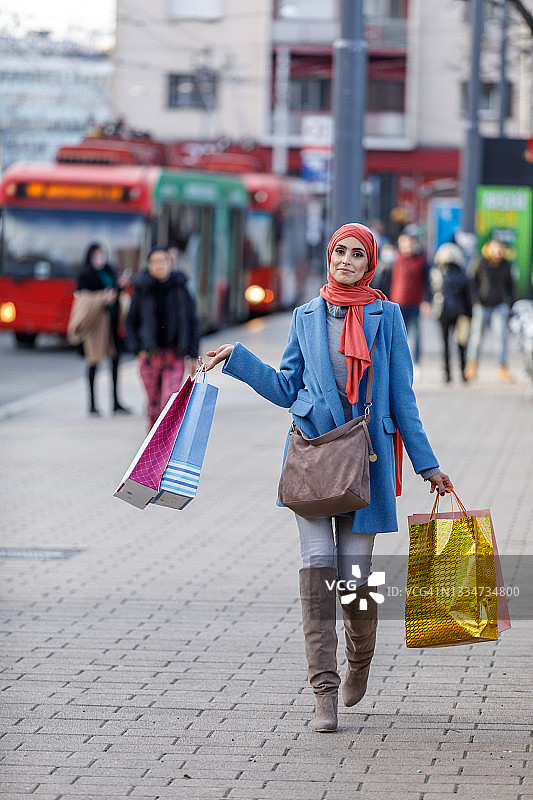 一名穆斯林妇女在城市街道上享受放松的购物日。图片素材