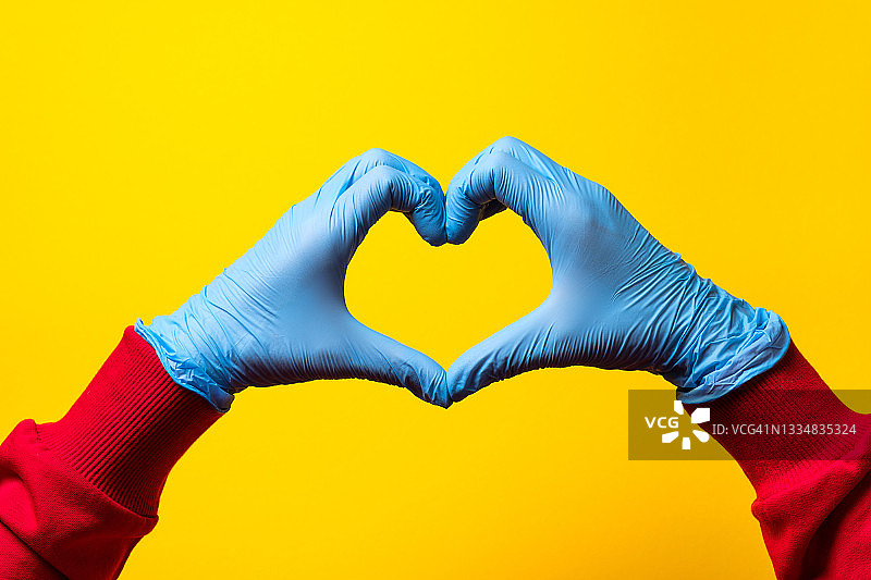 心形符号由戴着蓝色医用防护手套的心脏病专家、医务工作者、医生或实验室助理的手制作而成。照顾心脏的健康保健医学的概念，预防心脏病。图片素材