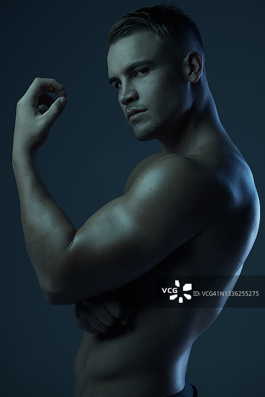 一名肌肉发达的年轻男子在黑暗的背景下赤裸上身图片素材