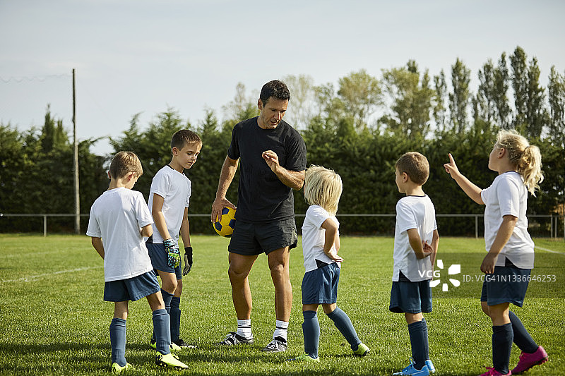 男教练在球场上向孩子们讲解足球图片素材