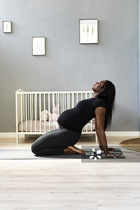 年轻的孕妇向后靠在卧室里练习瑜伽图片素材