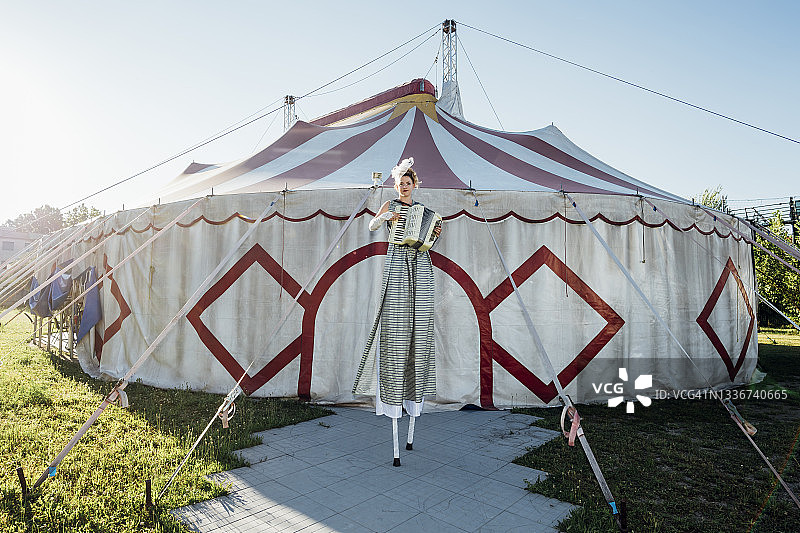 女马戏团演员，站在马戏团帐篷前的高跷上演奏手风琴图片素材