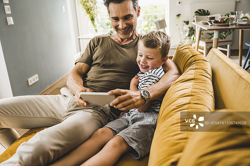 男人和儿子坐在沙发上玩智能手机图片素材