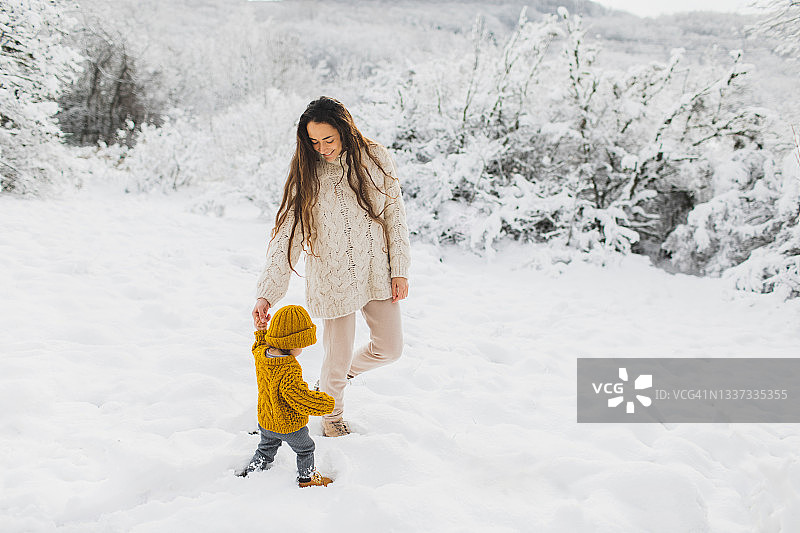 年轻的妈妈带着宝宝在雪天的森林里散步图片素材