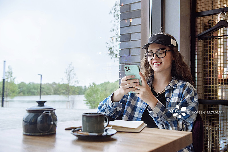 年轻快乐的女人坐在咖啡馆里，用电话和信使交流图片素材