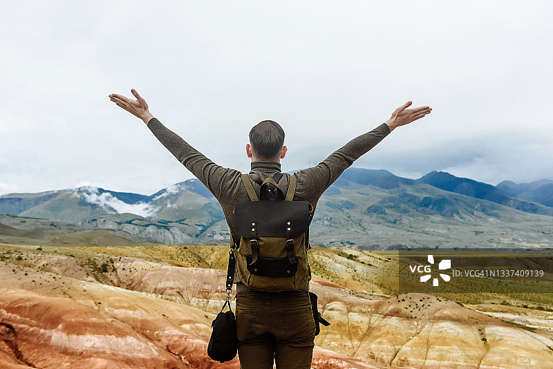 一个背着背包的徒步旅行者举起双手站在群山的背景上图片素材