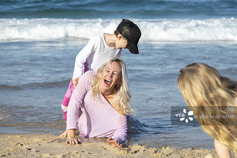 一个年轻的女人，母亲，带着她的两个孩子，儿子和女儿躺在沙滩上看着镜头，在一个阳光明媚的日子图片素材