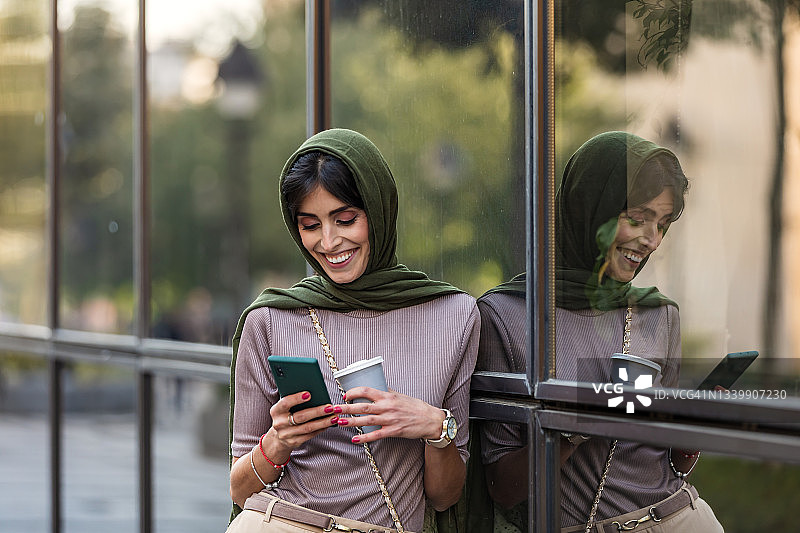 一个成熟的阿拉伯妇女在街上拿着一杯咖啡用手机图片素材