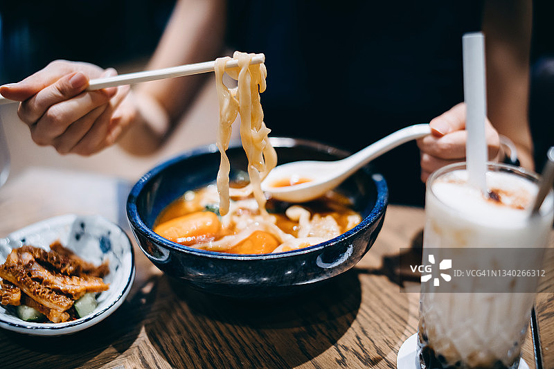 年轻的亚洲女人享受一碗台湾风格的牛肉面汤开胃菜和一杯冰奶茶在餐厅的特写。亚洲美食和饮食文化。外出就餐的生活方式图片素材