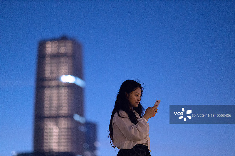 年轻的女商人在上海市中心的摩天大楼下使用智能手机图片素材