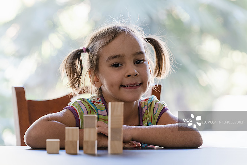 快乐的小女孩在家里玩木制玩具积木的肖像图片素材